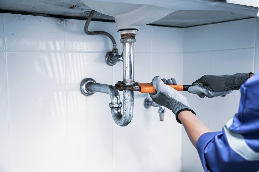 Plumber using a wrench to repair a sink pipe