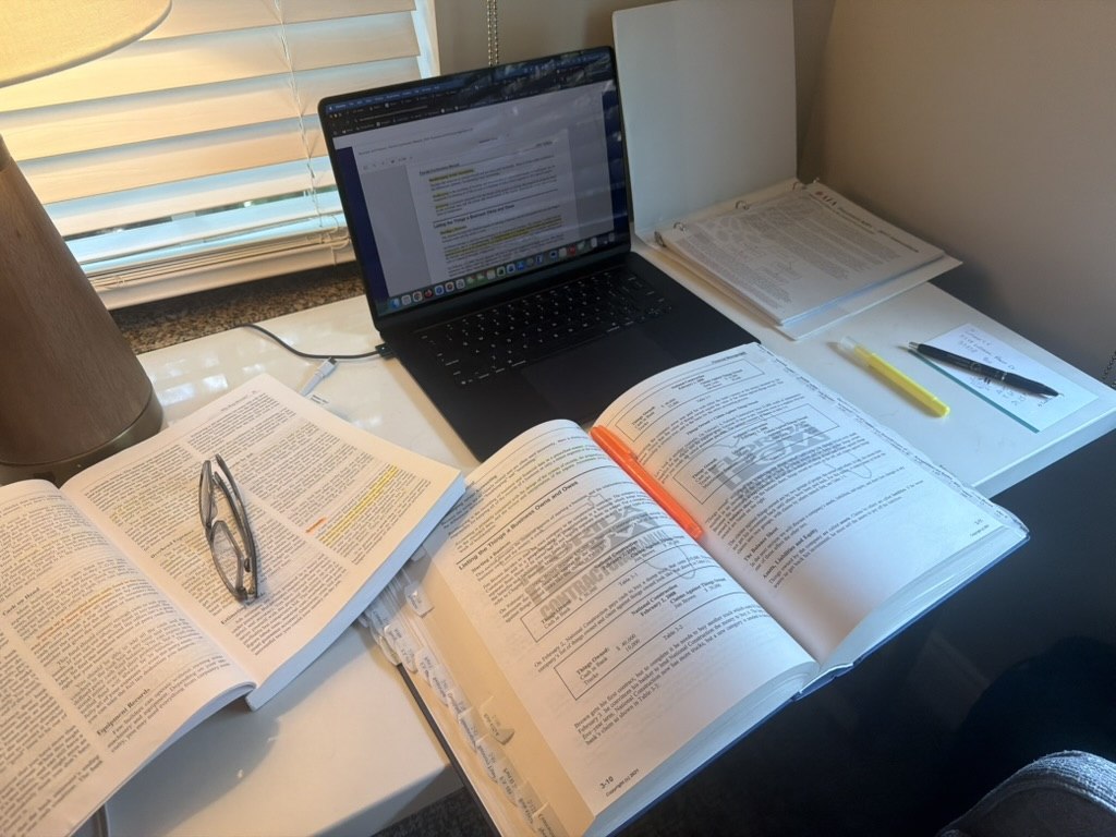 Open backflow course books, highlighted notes and a laptop on a study table