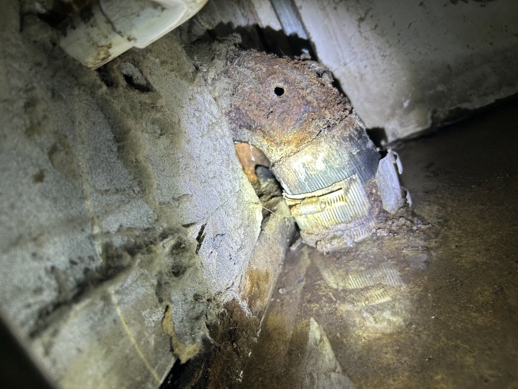 Damaged cast-iron fitting and connection exposed inside the bathroom wall