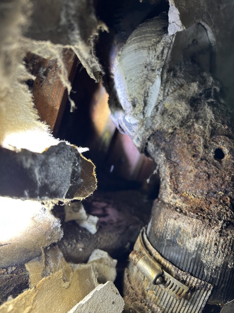 Corroded cast-iron drain piping surrounded by wall materials in a tight repair area