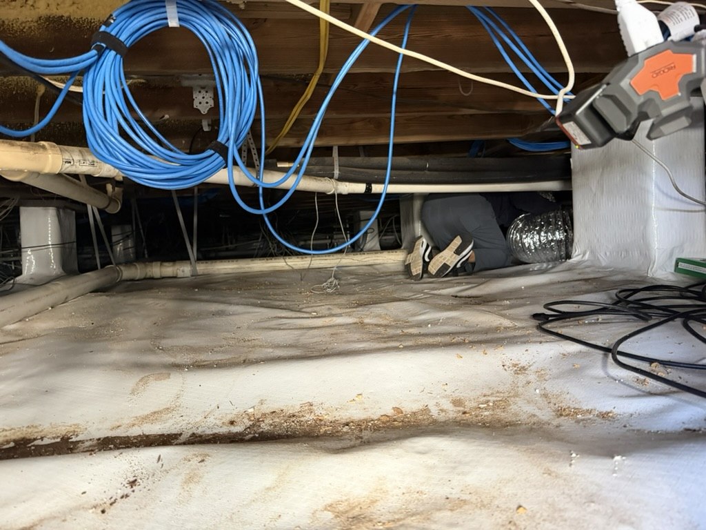 Advantage Plumbing team member working in the tight crawlspace beneath a medical office