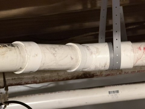 Drain piping held by a support strap beneath the building