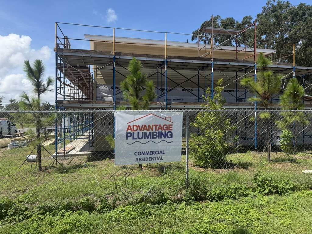 Building under construction with scaffolding and an Advantage Plumbing banner
