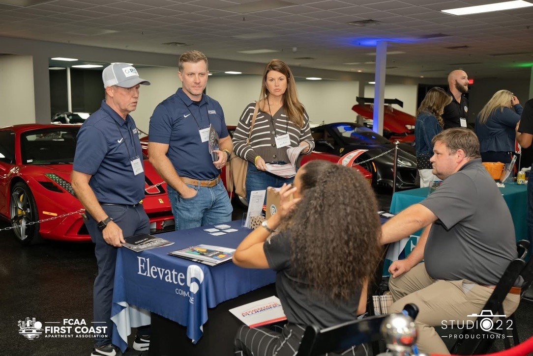 Attendees meeting with a management company at the FCAA 2026 Annual Business Exchange, with sports cars on display in the background