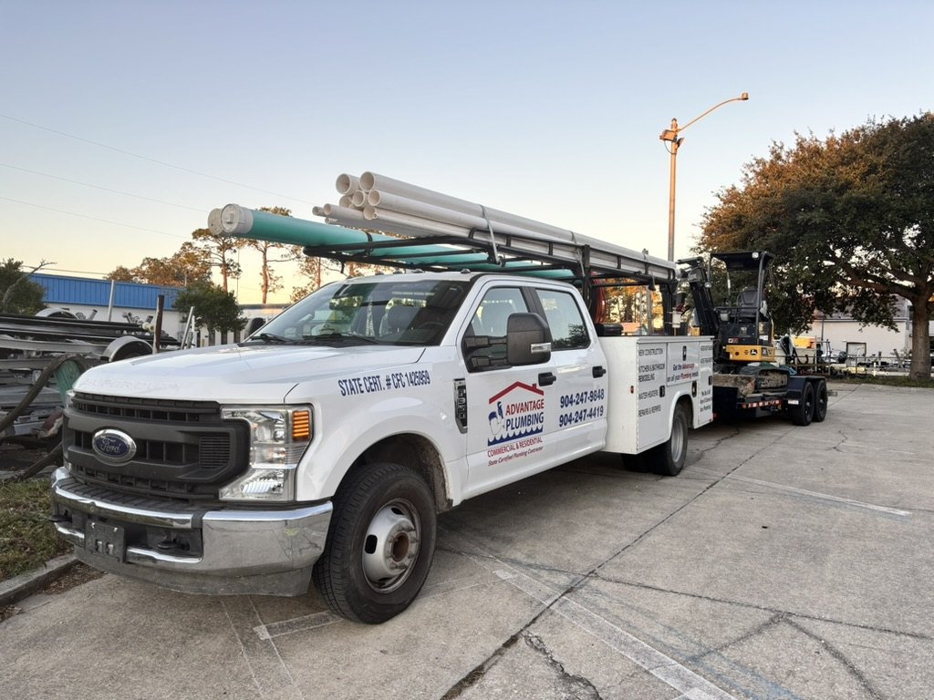 Advantage Plumbing service truck loaded with piping and towing an excavator
