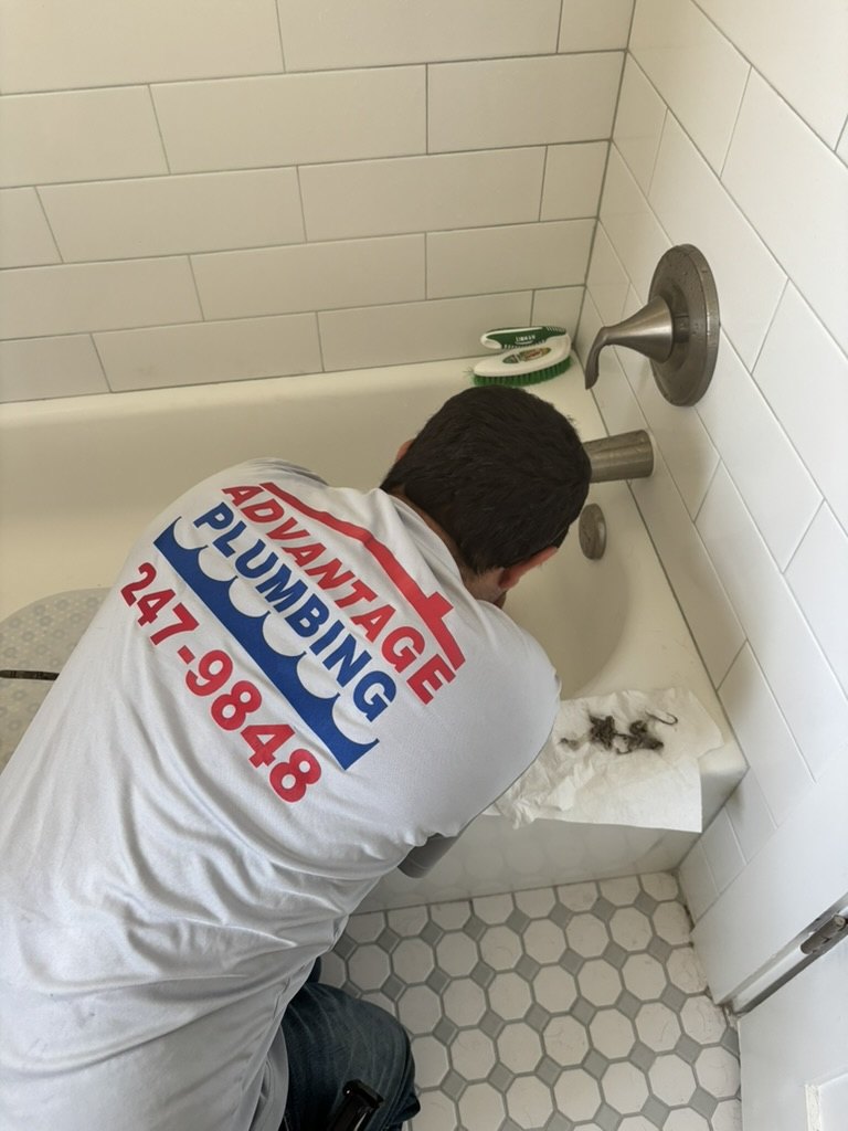 Advantage Plumbing technician clearing a bathtub drain, with removed hair beside the work area