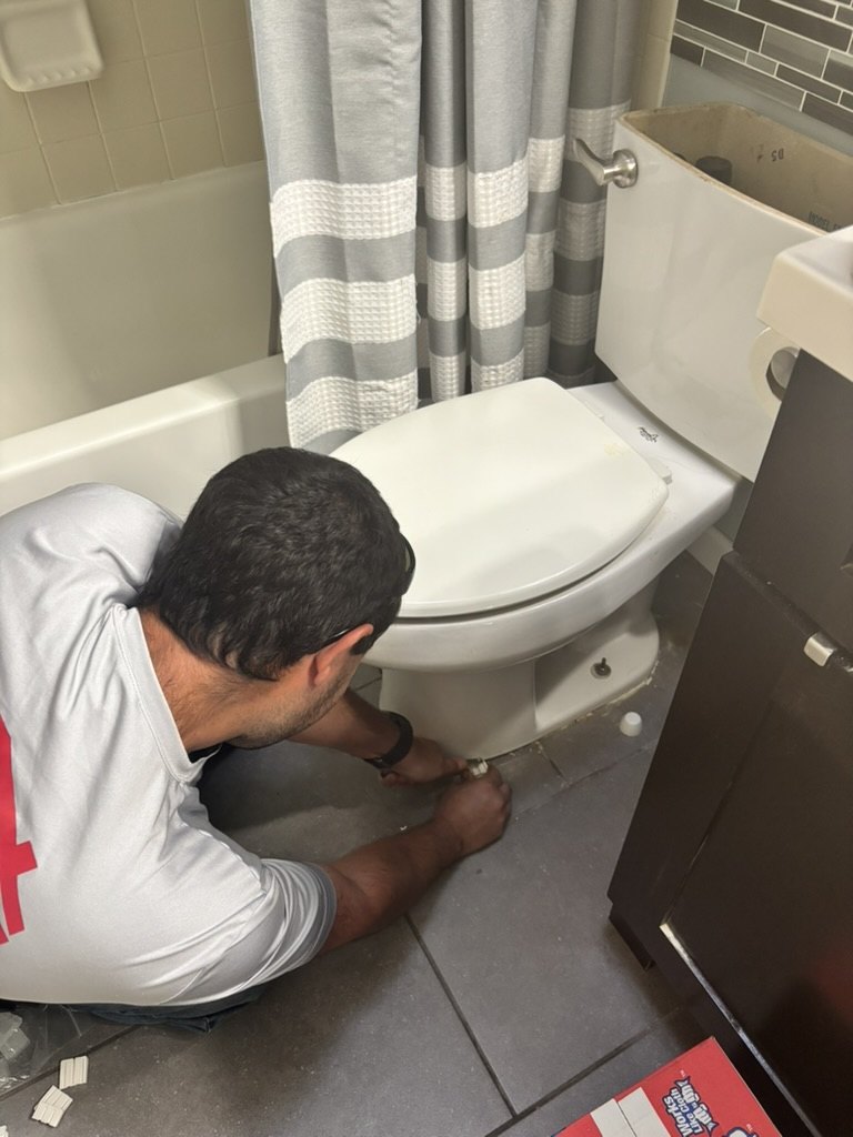 Advantage Plumbing technician working at the base of a wobbly toilet on a tiled bathroom floor