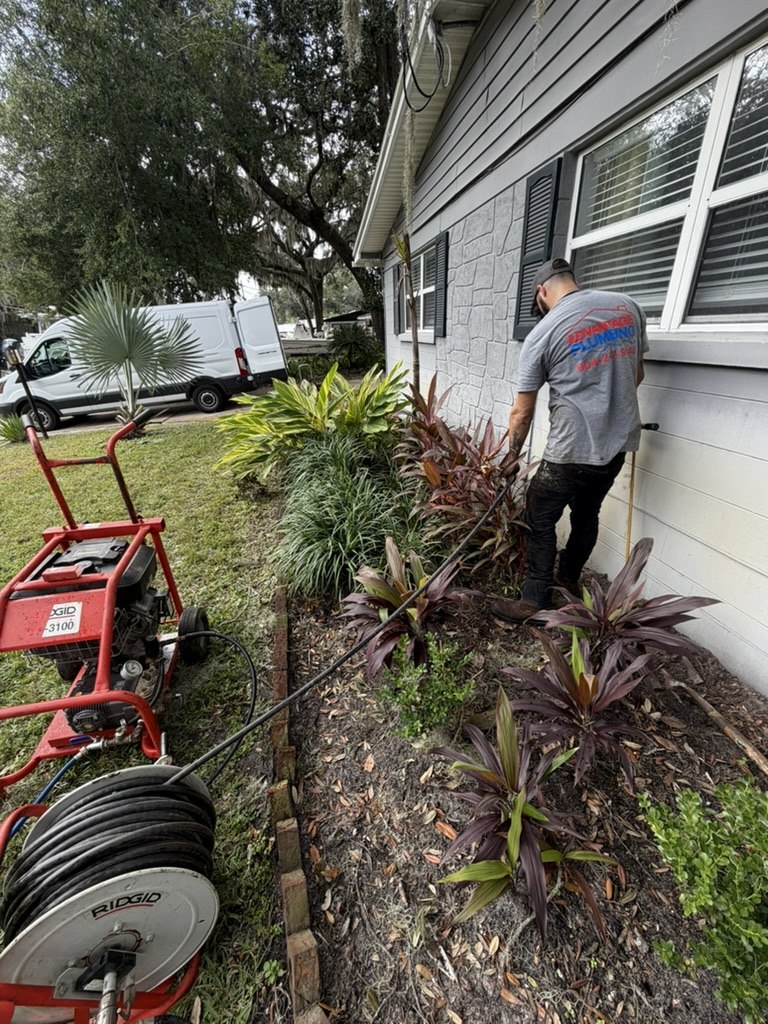Advantage Plumbing technician working beside the home with a water jetter and drain equipment nearby