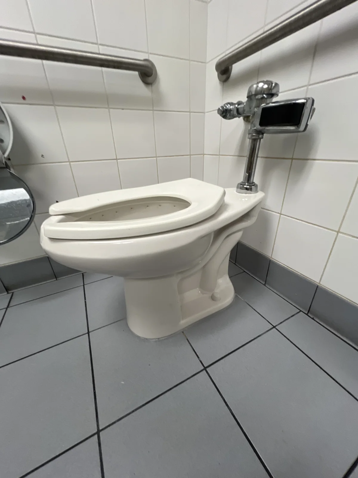 Side view of the school restroom toilet and its commercial flush valve