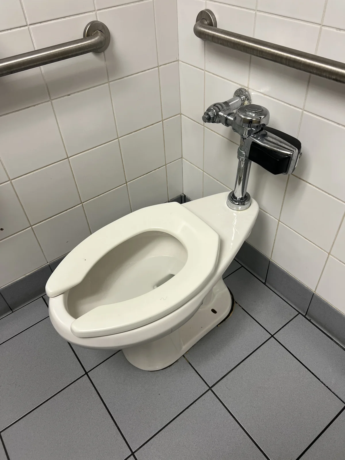 Commercial toilet and chrome flush valve in a tiled restroom at a local school