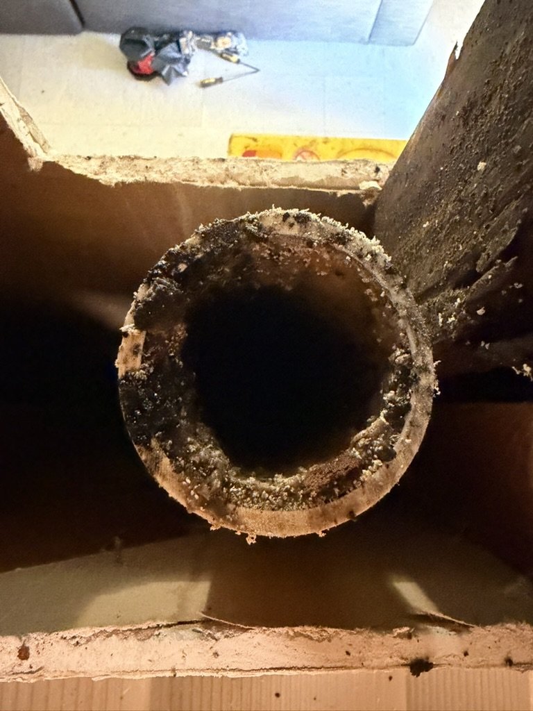 Cut end of existing cast-iron pipe visible between floor framing
