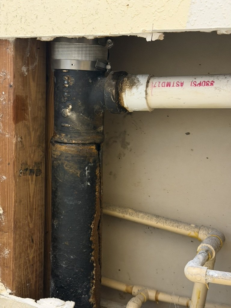 Existing cast-iron stack and fitting connected to PVC inside the opened wall