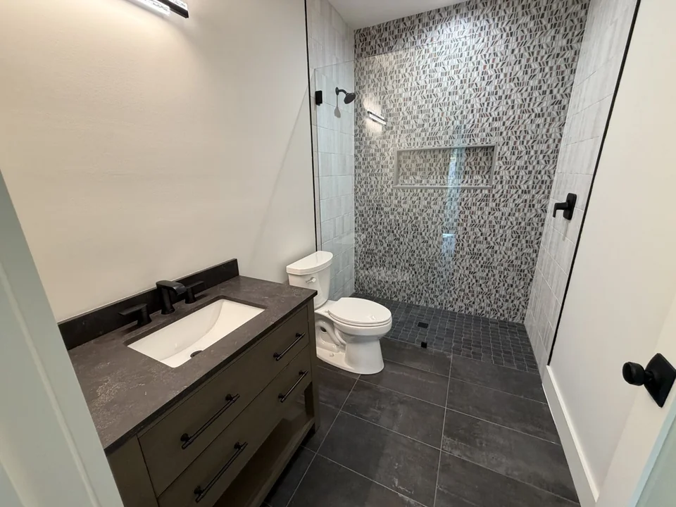 Completed bathroom with a vanity sink, toilet, and tiled shower installed by Advantage Plumbing